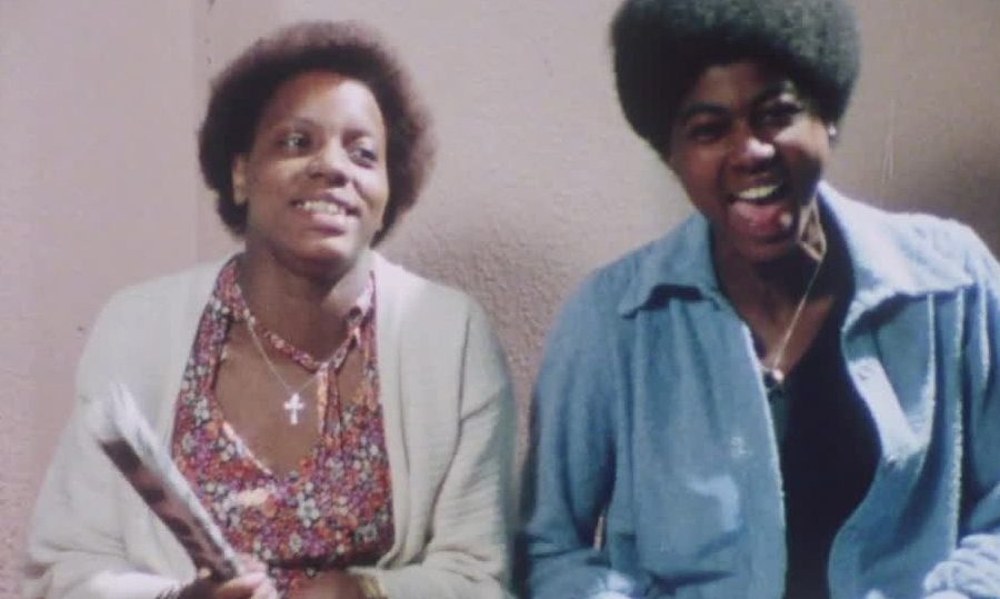 Still from the film Divide and Rule – Never! Showing two black teenagers looking at the camera mid conversation.