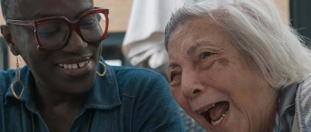 A picture of a Black woman in her 40s and a white woman in her nineties laughing together.