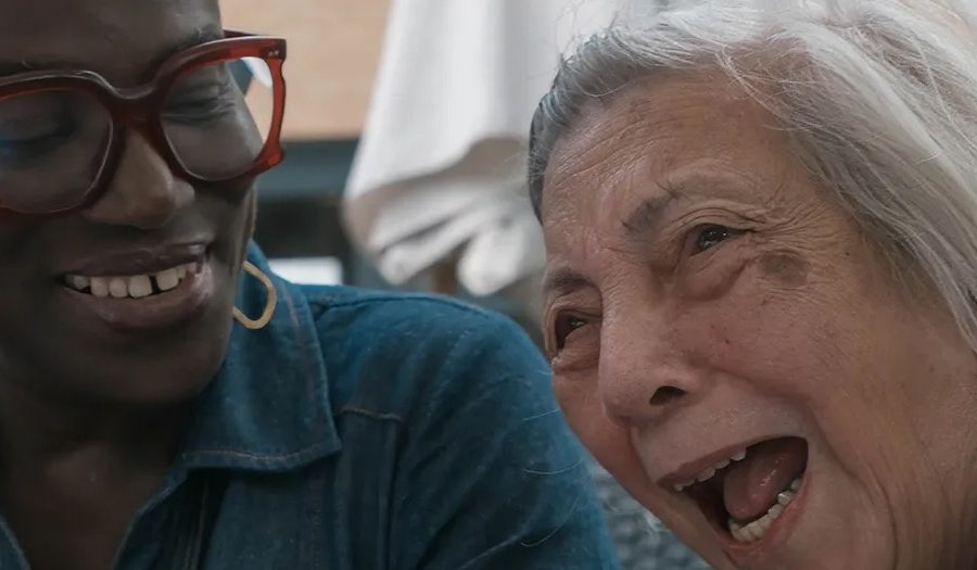 A picture of a Black woman in her 40s and a white woman in her nineties laughing together.