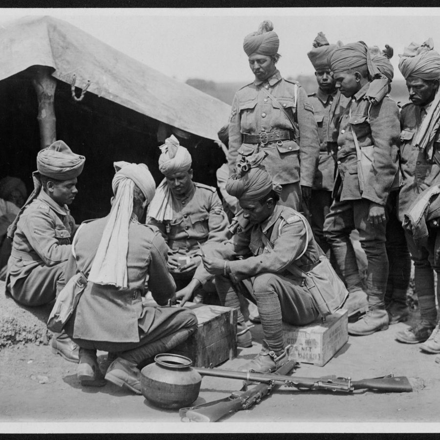 South Asian soldiers playing cards outside a tent. Rifles on the ground.