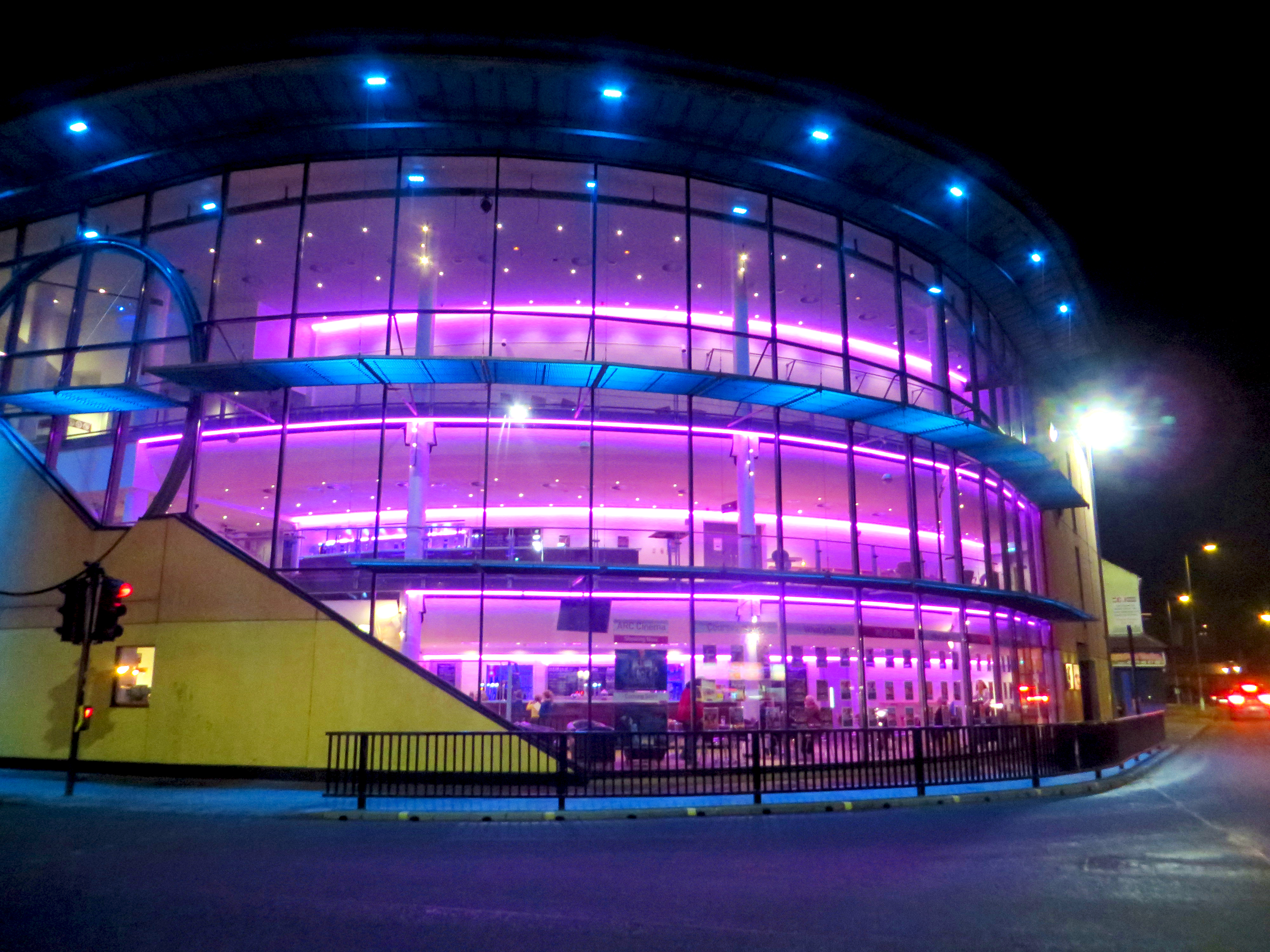 Glass-fronted modern building lit with blue and purple lights at night.