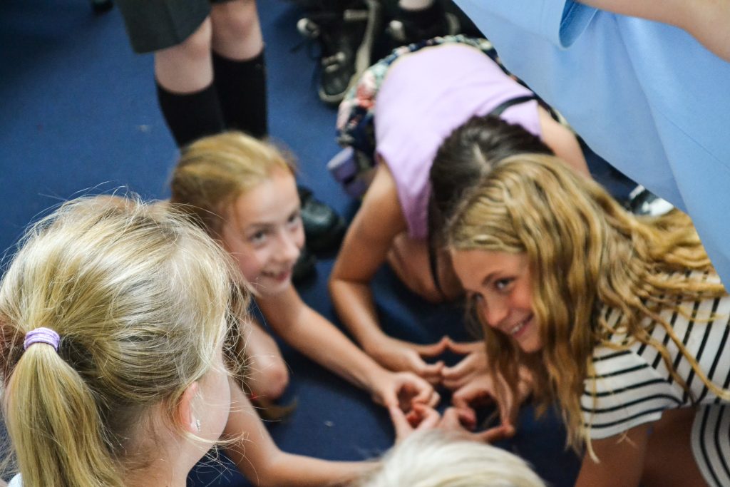 Children crouch in a circle making the shape of hearts with their hands