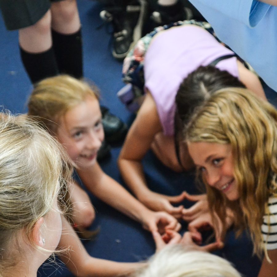 Children crouch in a circle making the shape of hearts with their hands