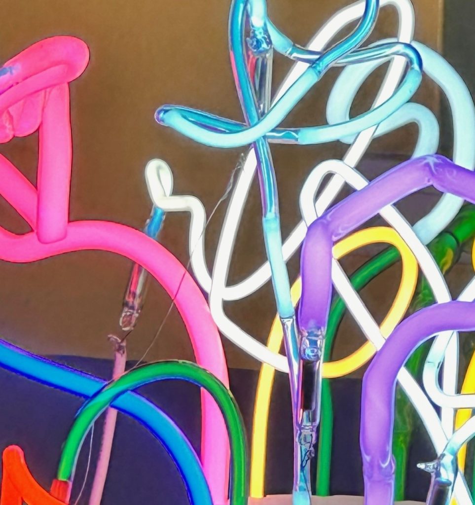 The image shows a closeup of colourful pieces of lit neon glass tubes overlapping each other