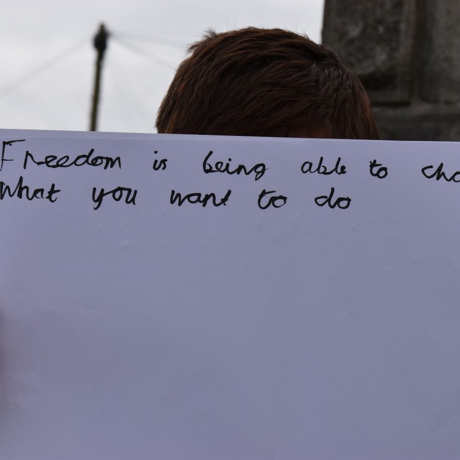 A person holding a large piece of paper in front of their face with text reading 'Freedom nis being able to choose what you want to do'