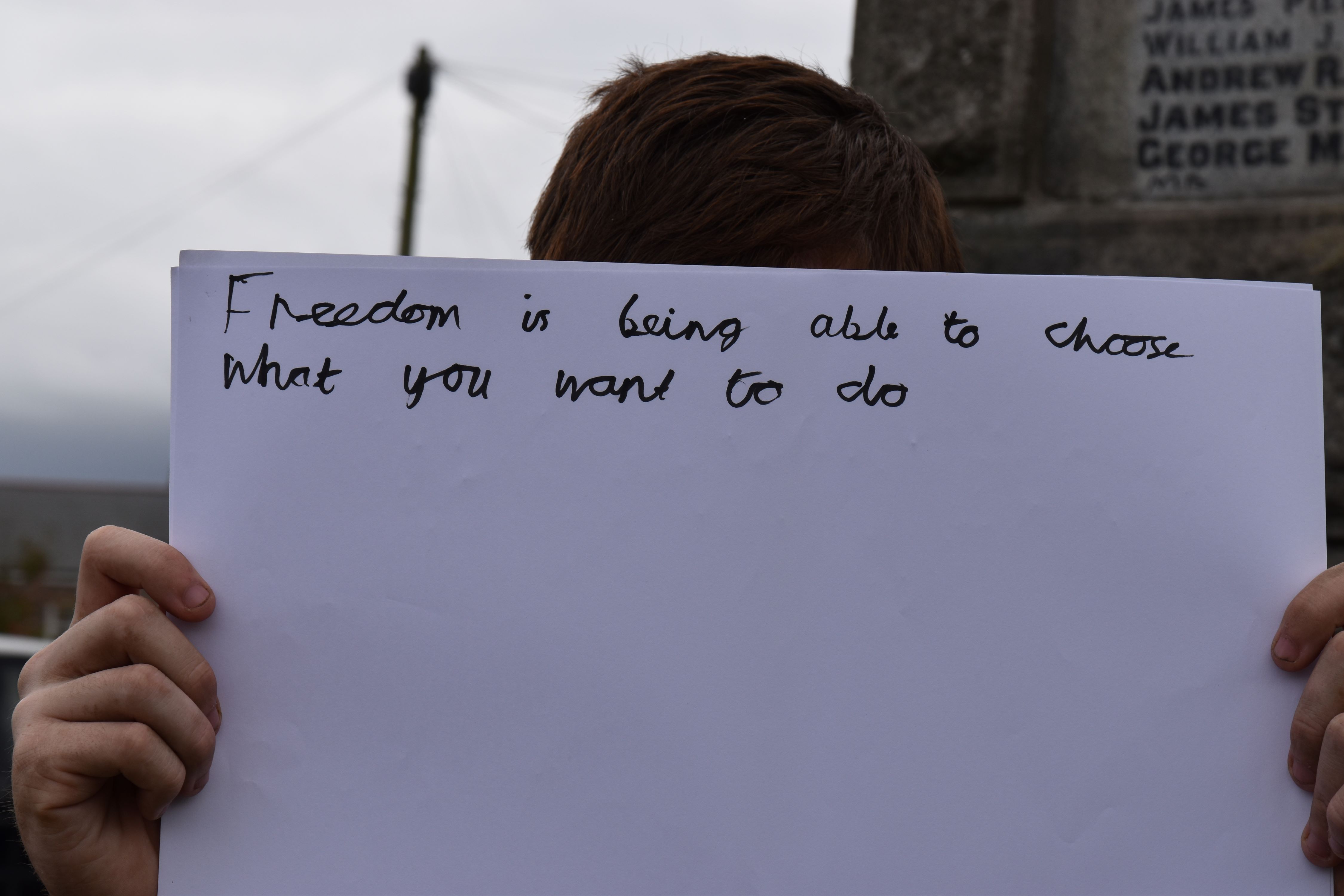 A person holding a large piece of paper in front of their face with text reading 'Freedom nis being able to choose what you want to do'