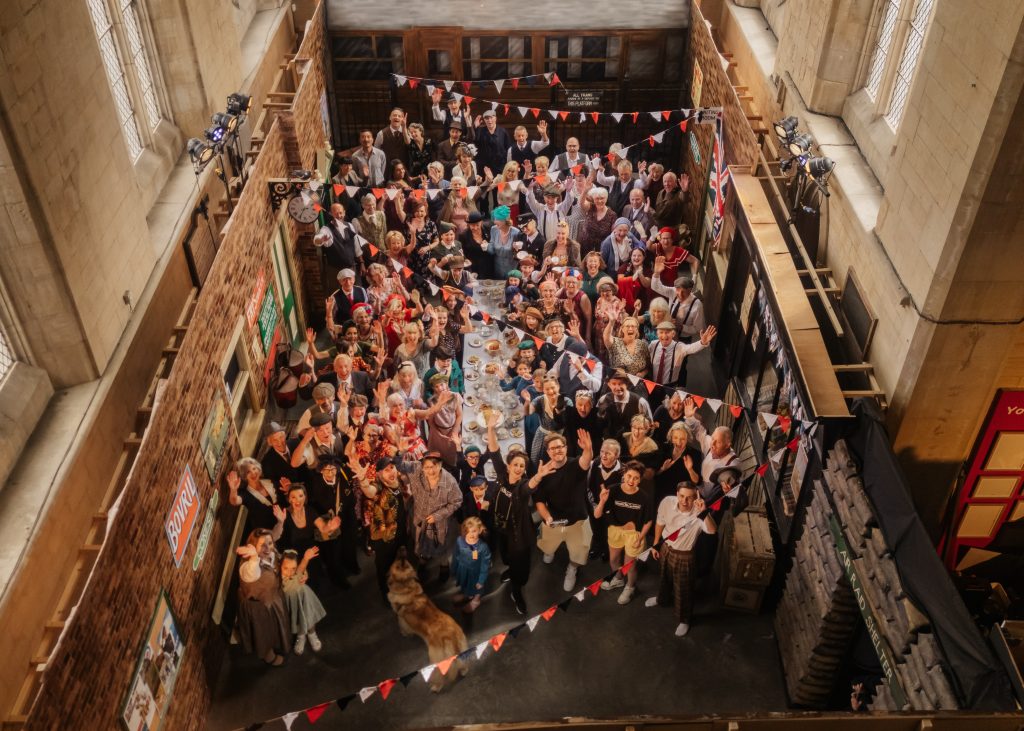 Images show a group of people in 1940s clothes around a street party with bunting