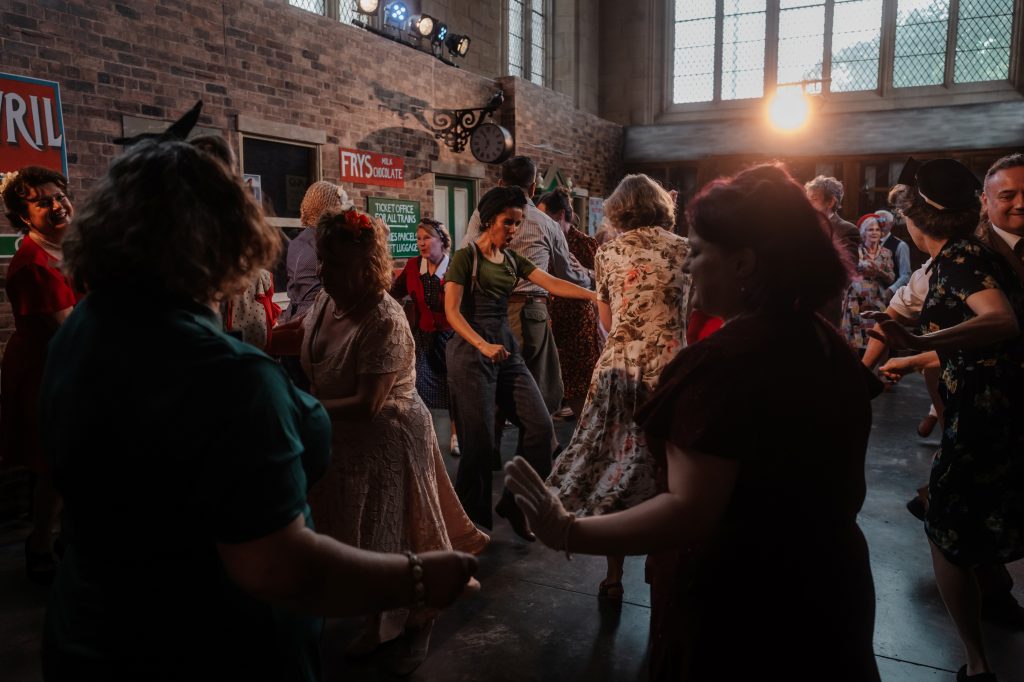 Images show a group of people in 1940s clothes dancing in the Lindy Hop style in a train station filmset at 20-21 Visual Arts Centre