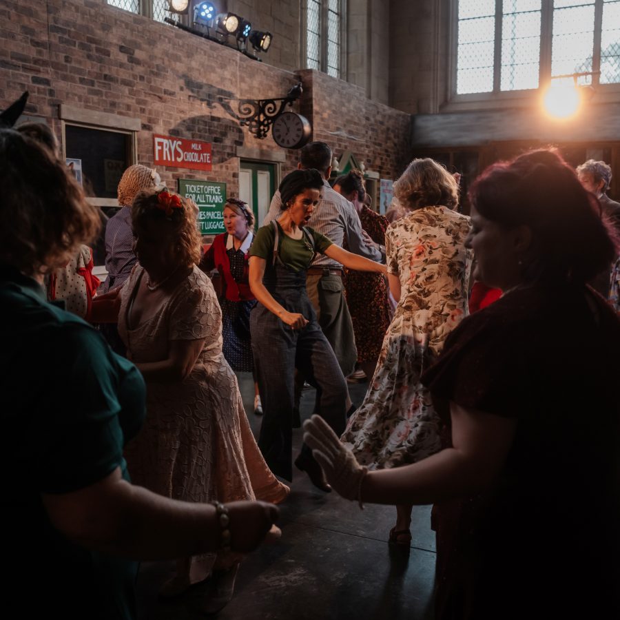 Images show a group of people in 1940s clothes dancing in the Lindy Hop style in a train station filmset at 20-21 Visual Arts Centre